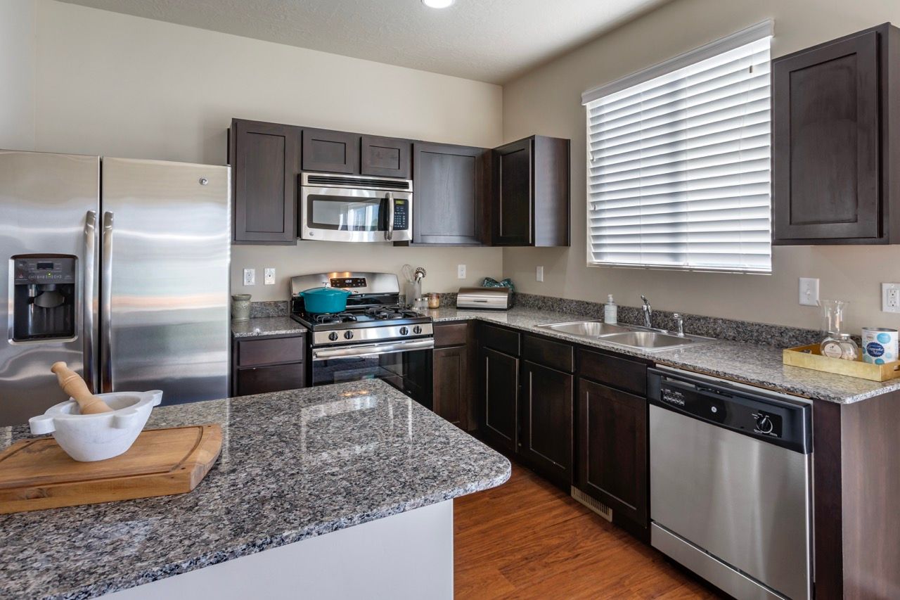 Open kitchen in a modern apartment with stainless steel fridge, microwave, stove, dishwasher, and granite countertops.