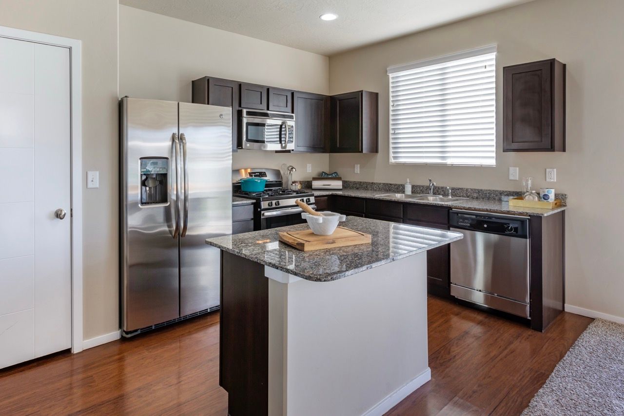 Modern kitchen with stainless steel fridge, range, microwave, granite countertops, and an island.