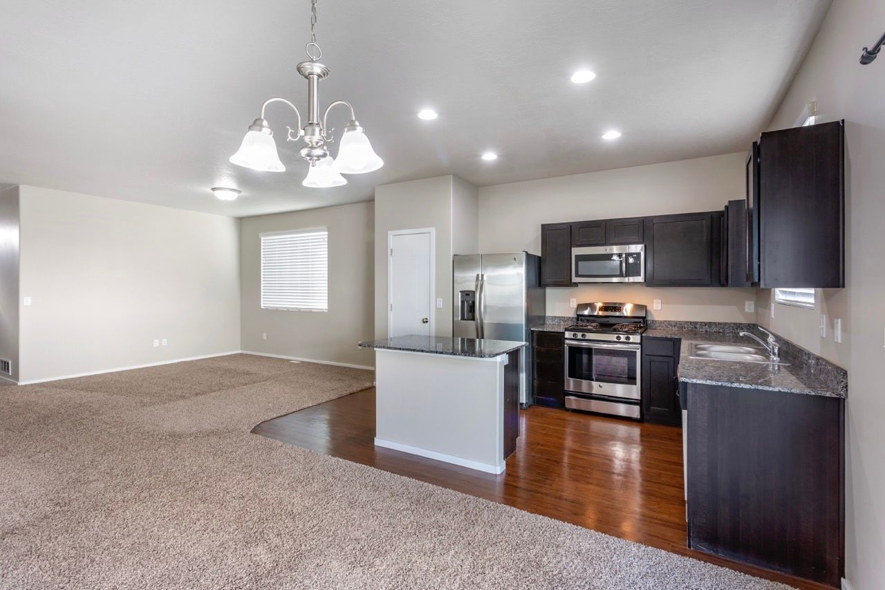 Open-concept kitchen with island, granite countertops, dark cabinets, stainless steel appliances, and adjacent living area.