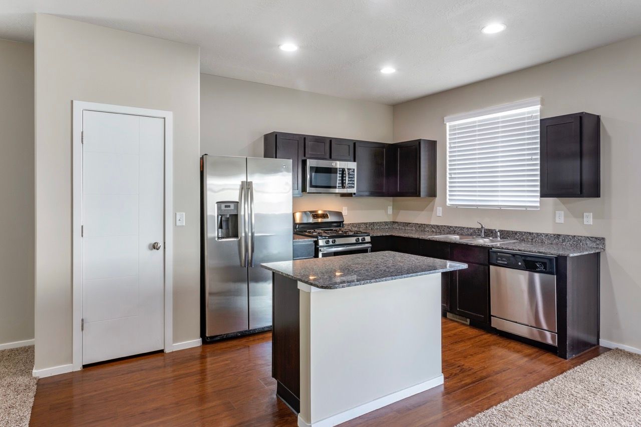 Modern apartment kitchen with stainless steel fridge, range, microwave, and granite-topped island.