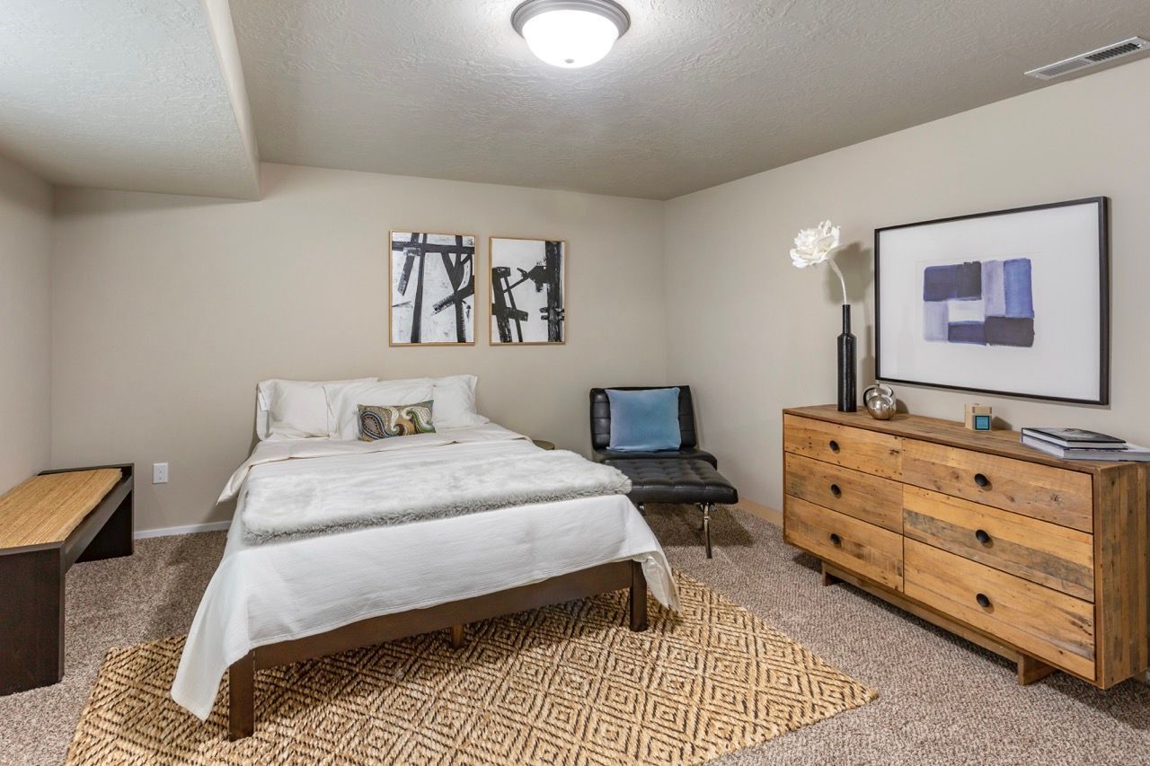 Bedroom in an apartment with a bed, dresser, chair, rug, and wall art.