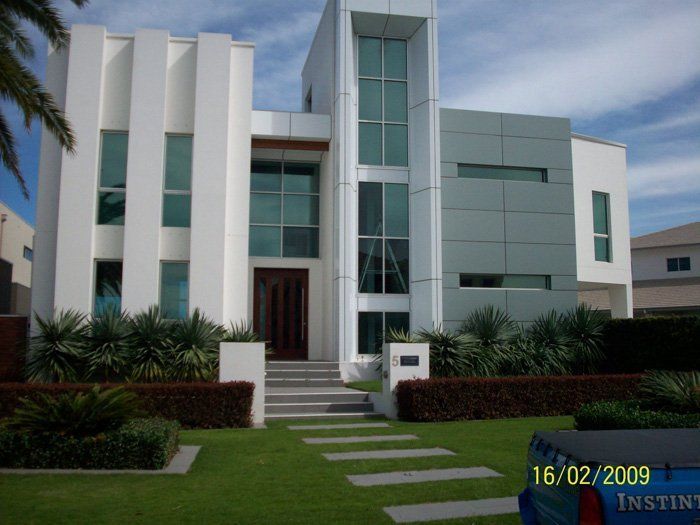 Modern white and grey house with large windows, set on manicured lawn.