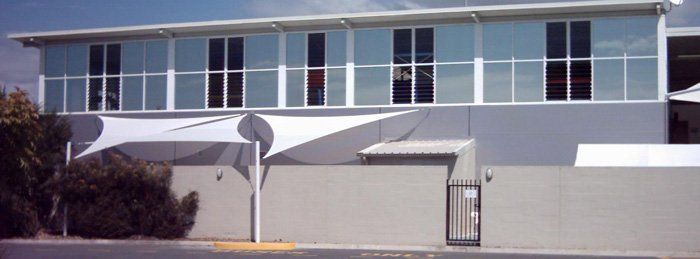 A modern building with large windows and a white sunshade over a lower-level wall.