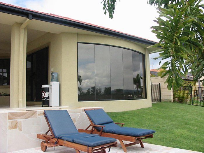 Two blue lounge chairs on patio, with view of home with large, curved windows and green lawn.
