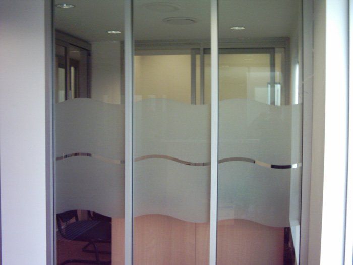 Glass office doors with frosted wave pattern, silver frames. Interior room, chair visible.