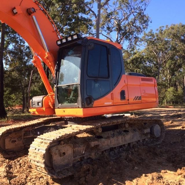 Orange excavator on a muddy construction site, surrounded by trees.
