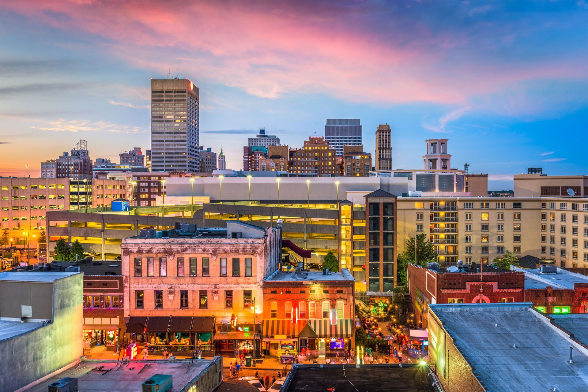 City skyline at sunset with pink and blue sky, lit buildings.