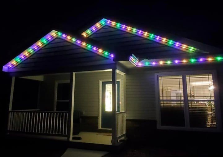 House at night with colorful LED lights outlining the roof, porch, and doorway.