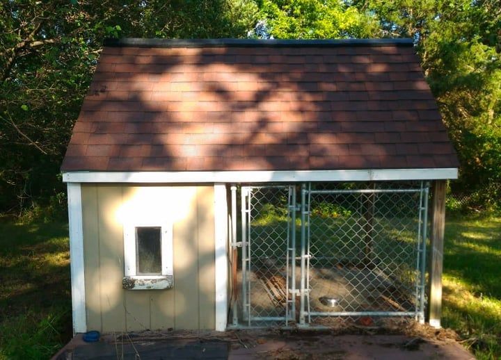 Dog house with a brown roof and a fenced-in yard.