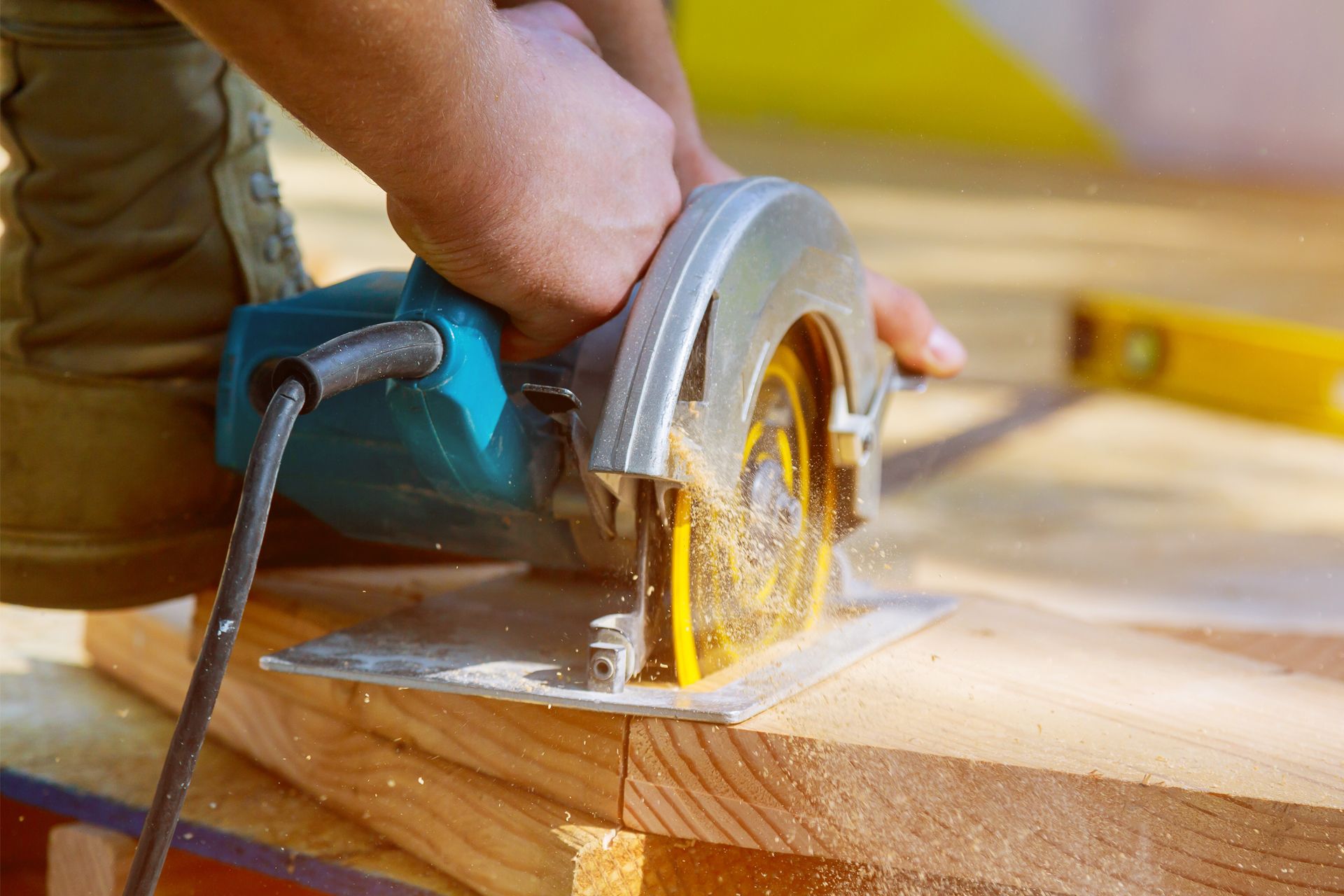 Person using a blue circular saw to cut wood on a construction site, outdoors.