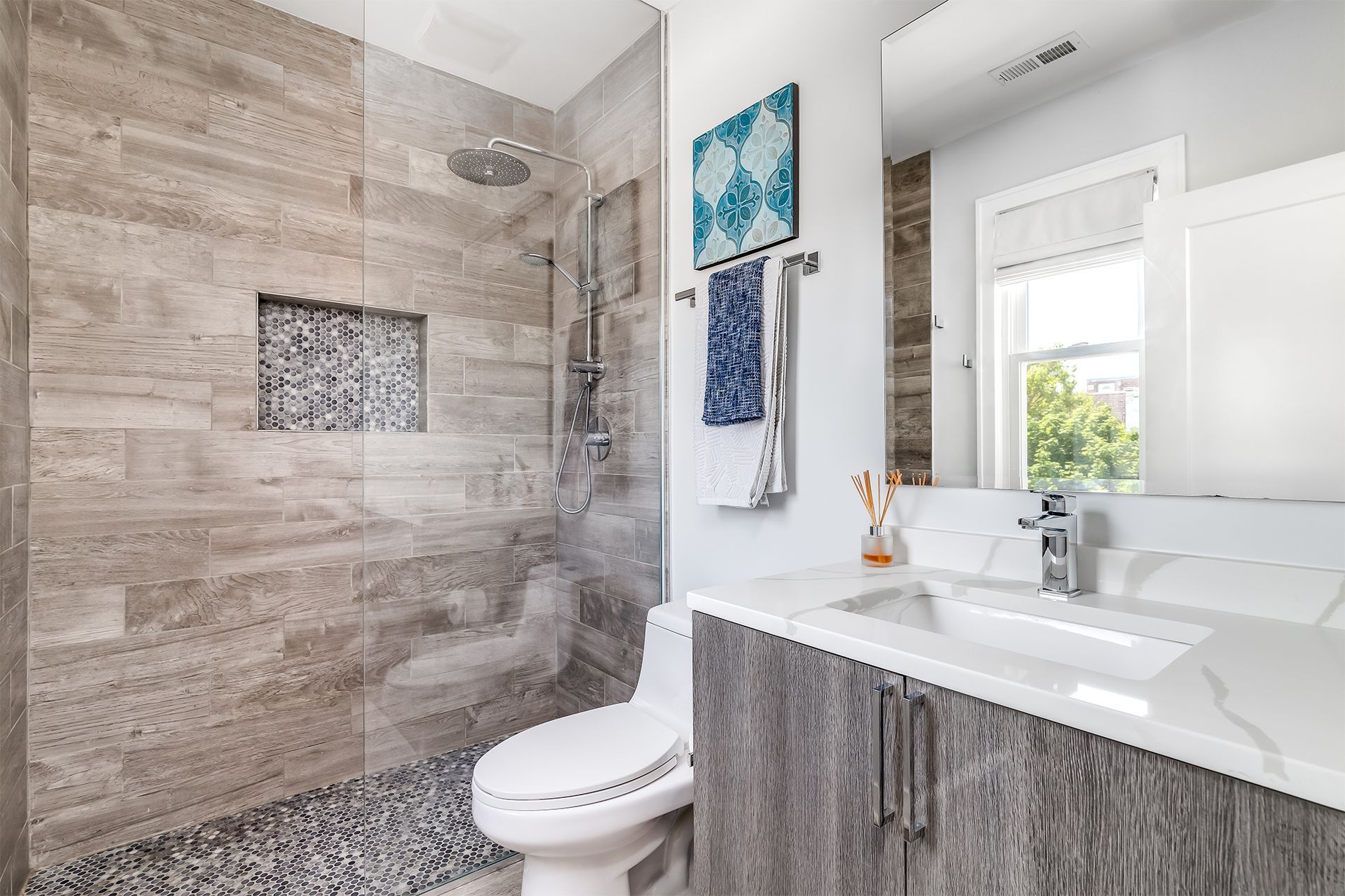 Bathroom with stone tile shower, gray vanity, and white toilet.