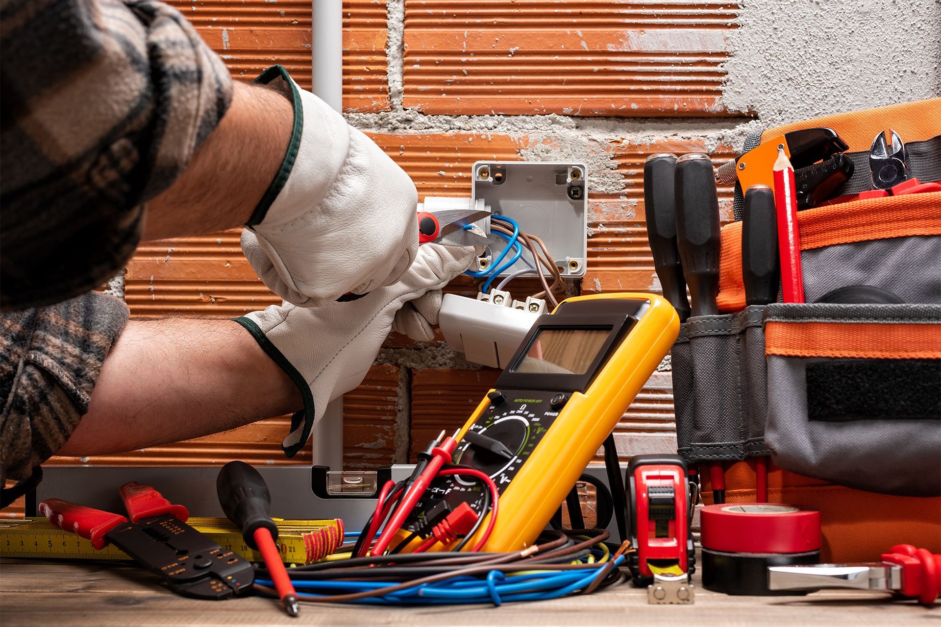Electrician working on wiring in an orange brick wall.