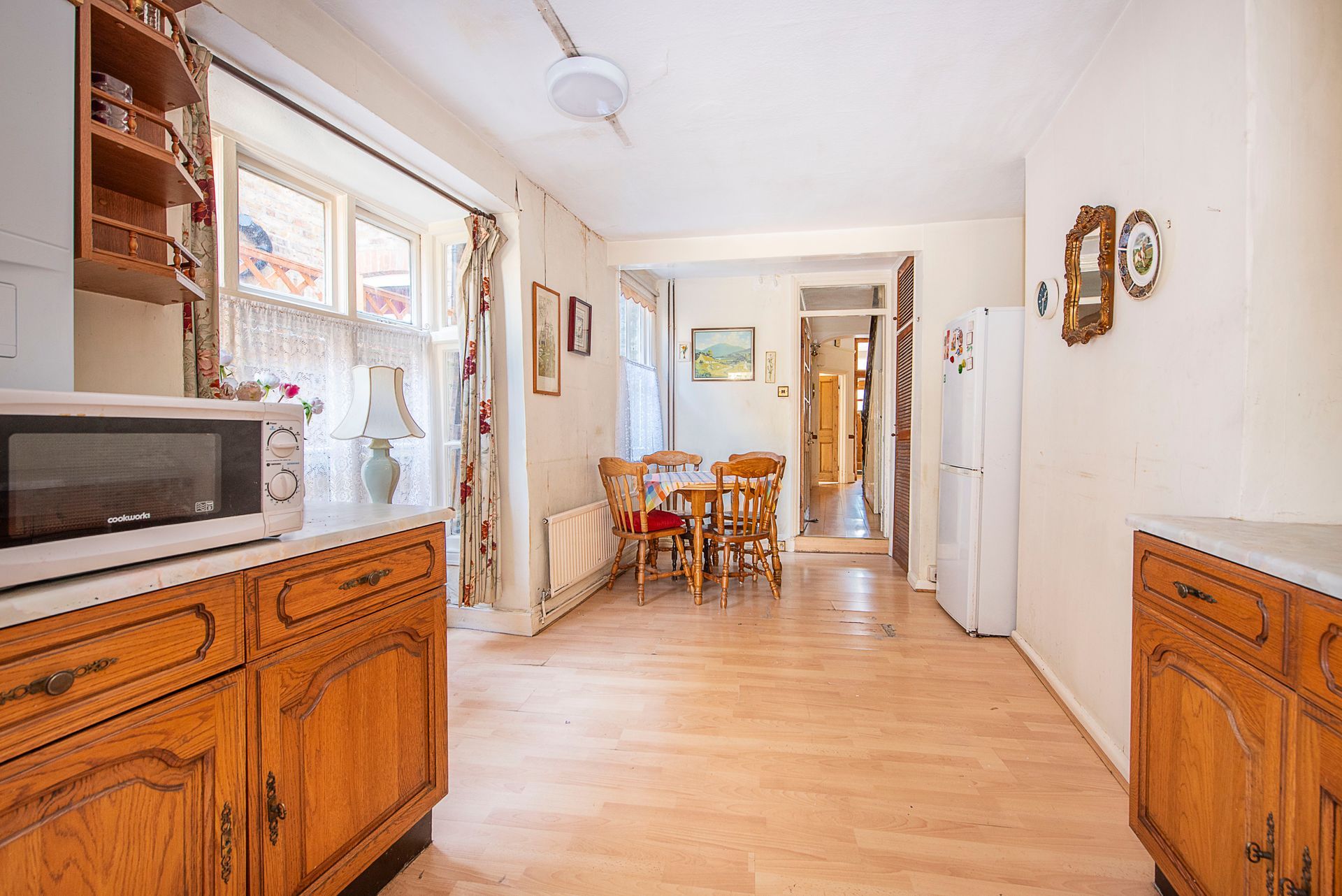 Kitchen with wood cabinets, microwave, table, window, and doorway leading to another room.