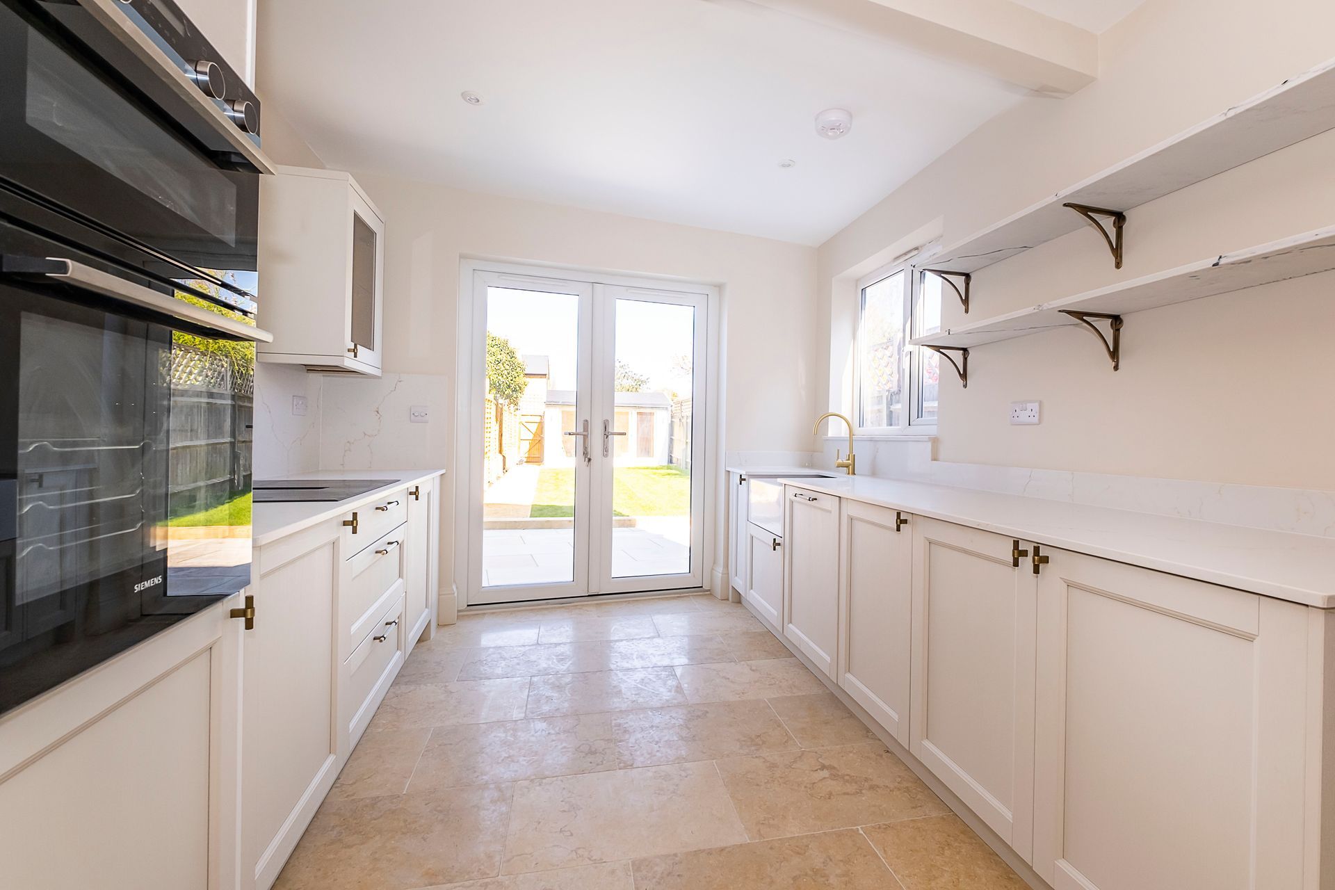 Cream-colored kitchen with cabinets, countertops, and appliances. French doors lead to a yard.