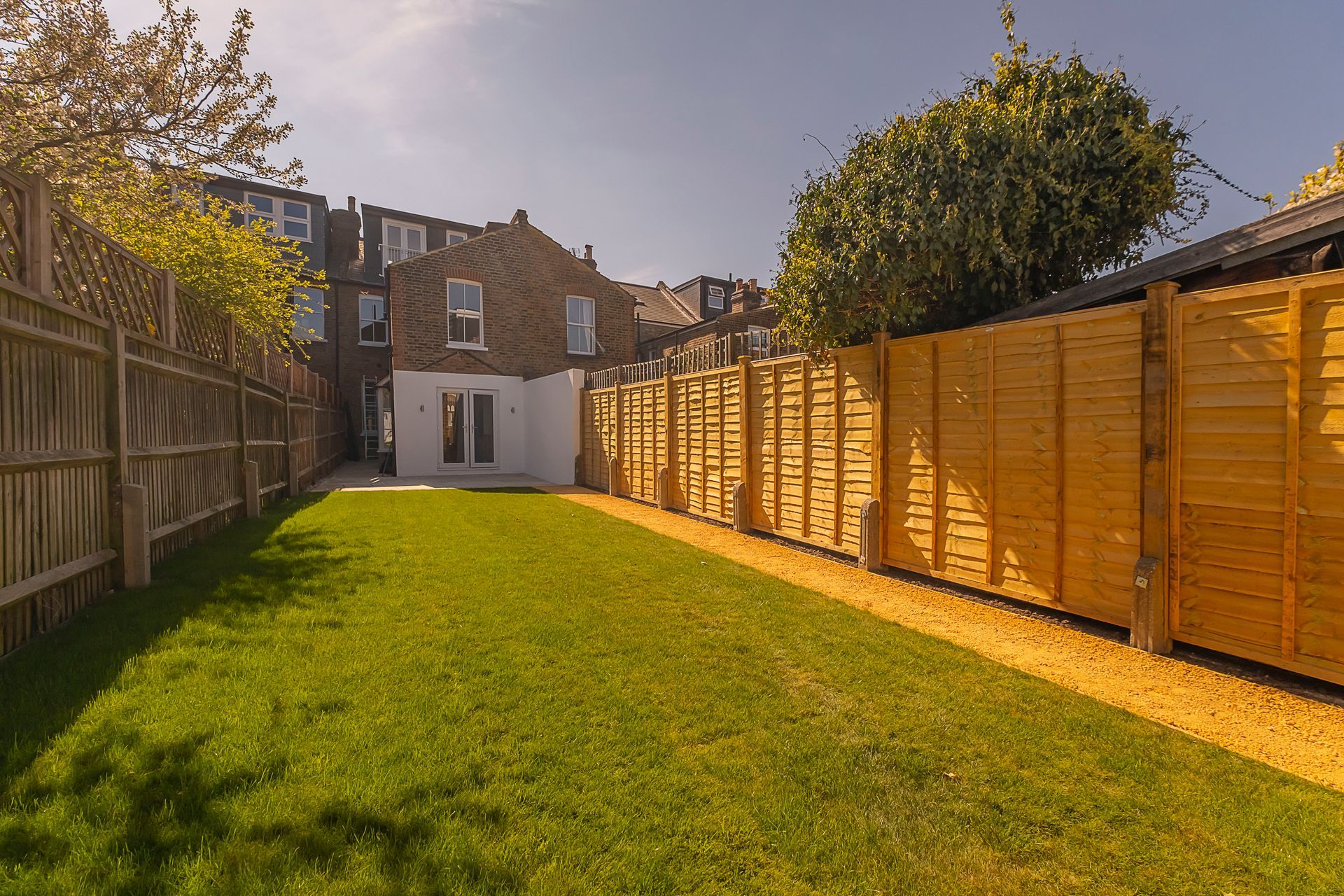 Backyard with green grass, wooden fences, and a house in the background on a sunny day.