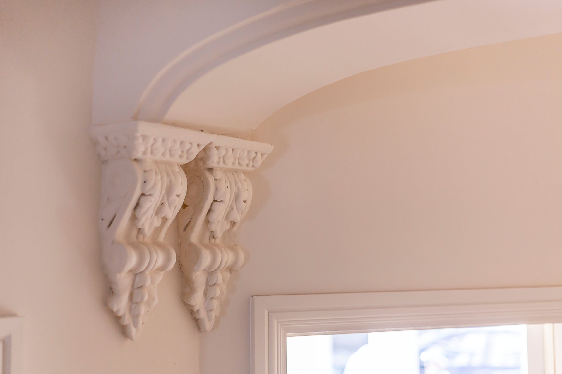 White decorative corbels supporting an arched ceiling in a room with a window.