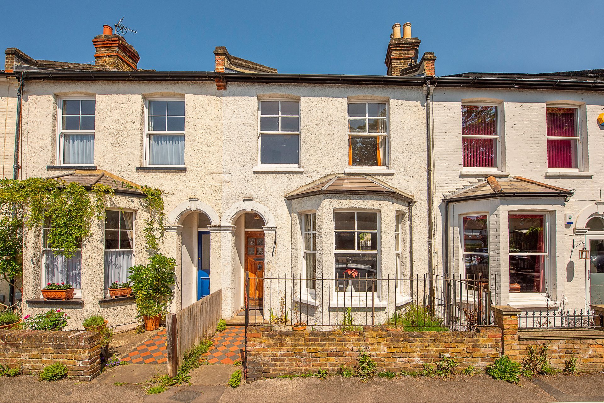 Row of white brick houses with varying window styles and colored curtains under a bright blue sky.