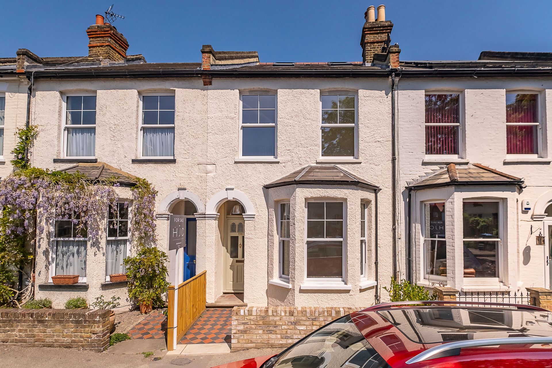 Row of white terraced houses with bay windows; red car in front.