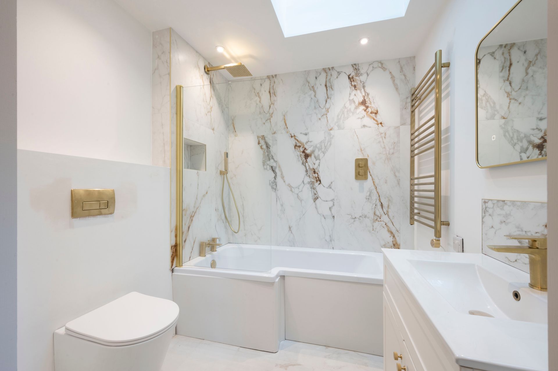 Elegant white bathroom with marble accent wall and gold fixtures.