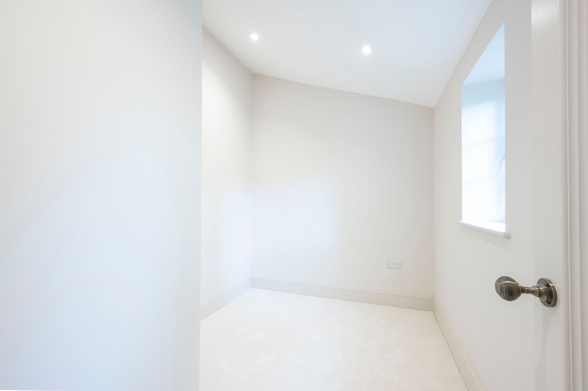 Empty, small, white room with a window on the right. A doorknob is visible.