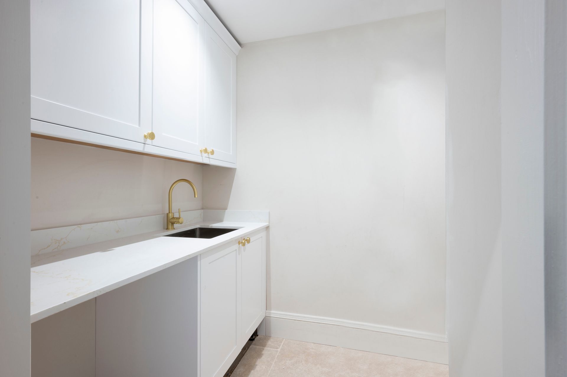 White laundry room with sink, cabinets, and gold faucet.