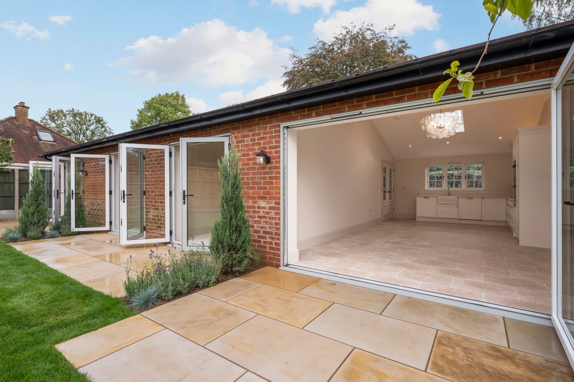 Exterior of a brick building with open folding doors, patio, and green lawn.