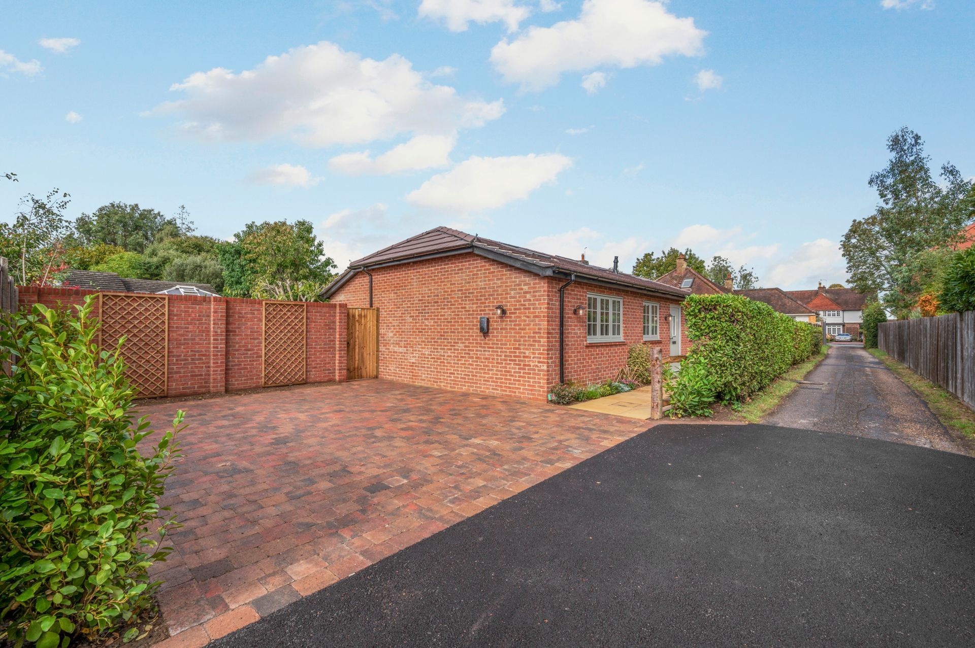 Brick bungalow with brick-paved driveway, wooden fence, and small asphalt driveway on a sunny day.