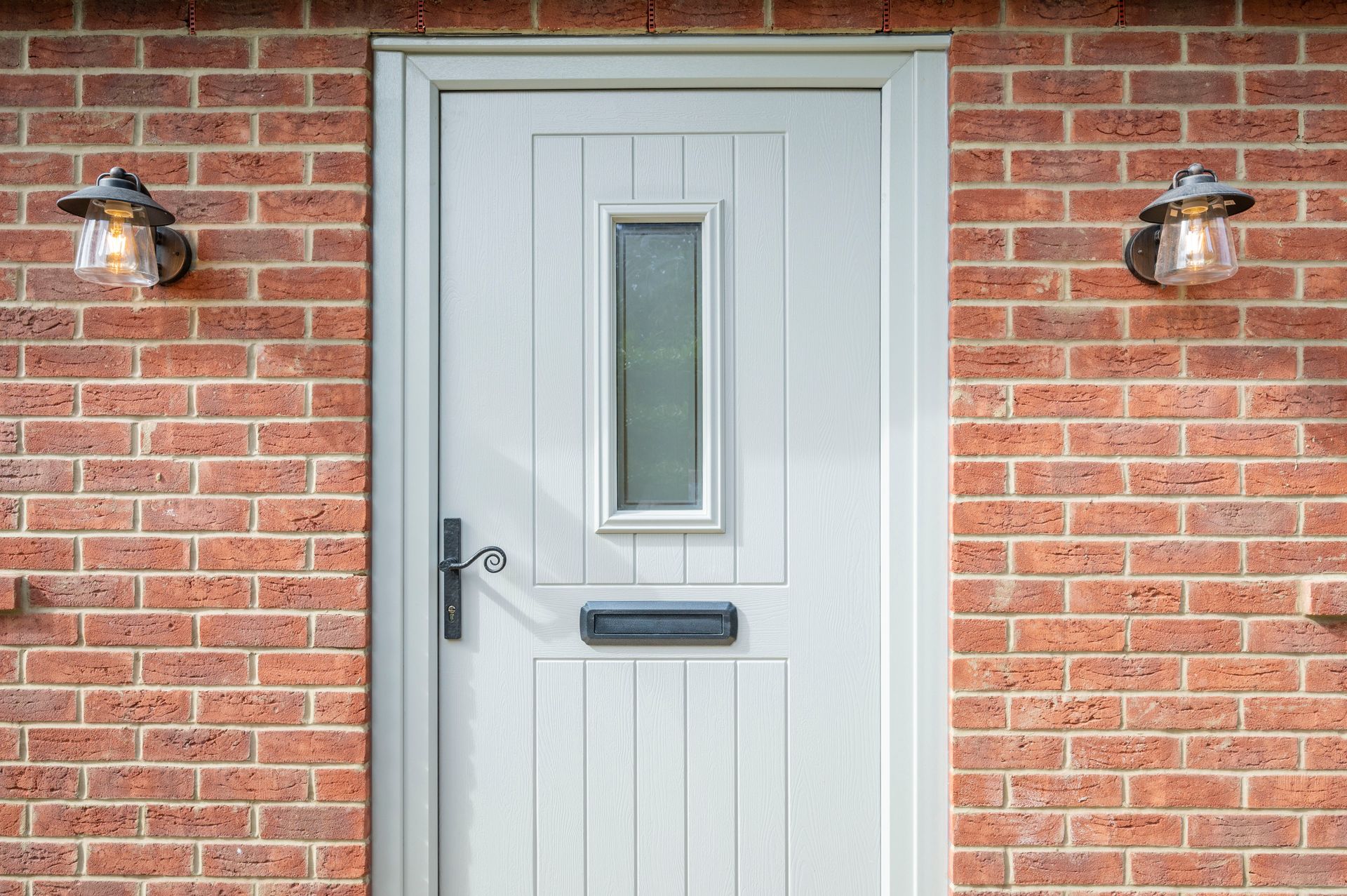 White door with glass pane and mailbox, framed by brick wall and sconce lights.