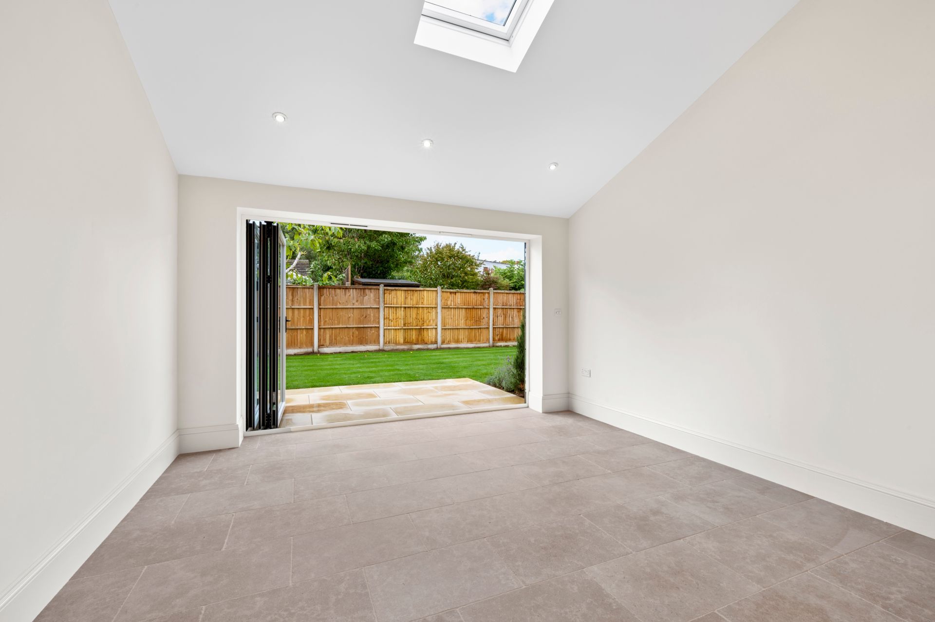 Empty room with open doors to a backyard. Beige carpet, white walls, skylight.