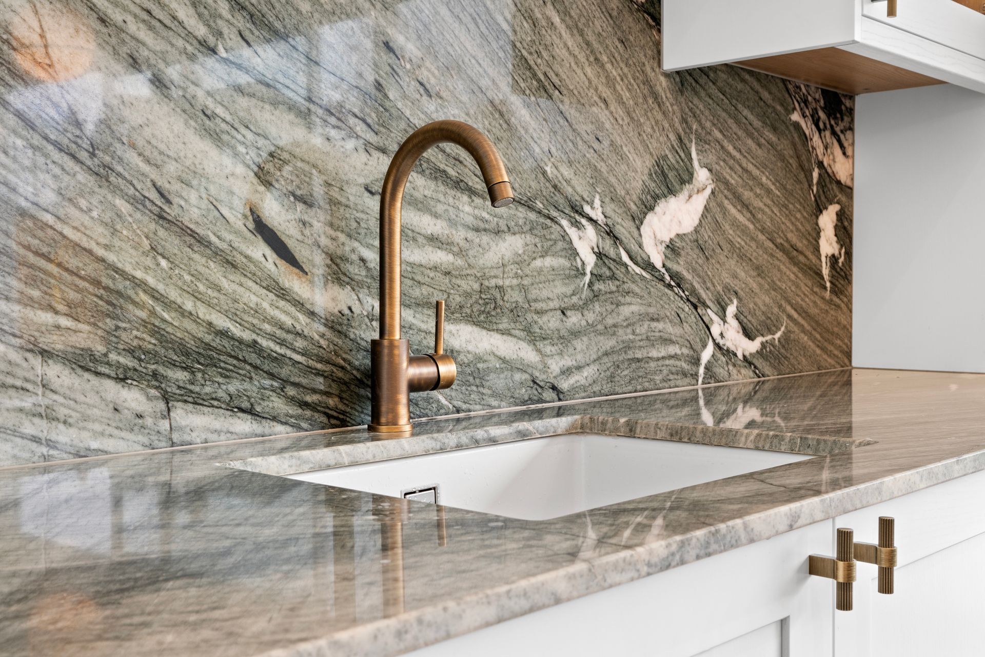A kitchen sink with a marble counter top and a brass faucet.