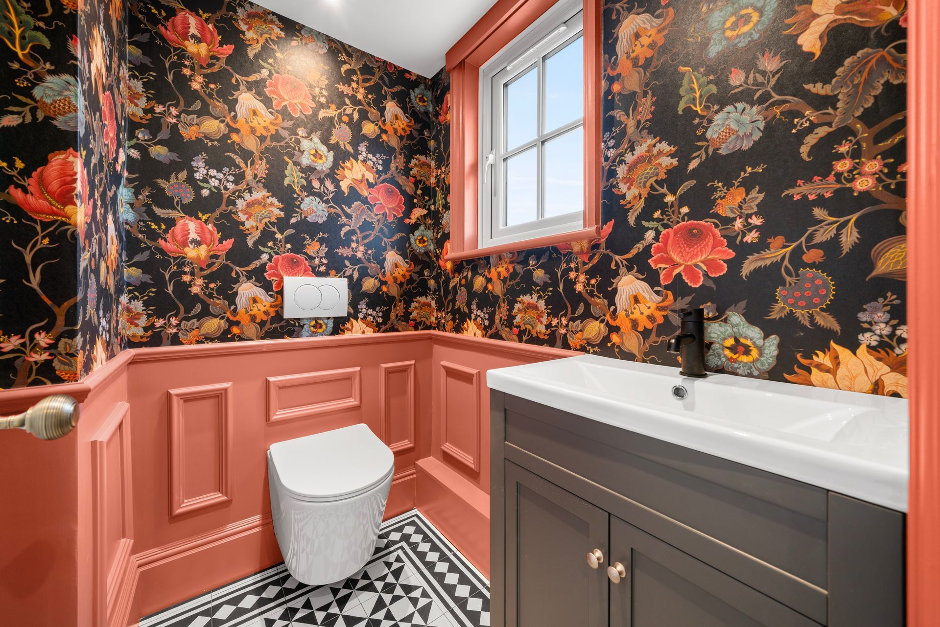 A bathroom with a toilet , sink , and floral wallpaper.