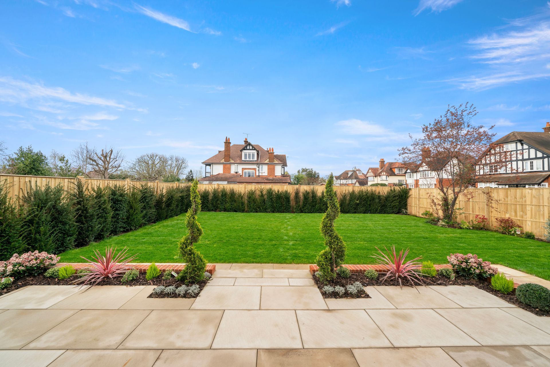 A large lawn with a patio in the foreground and a house in the background.