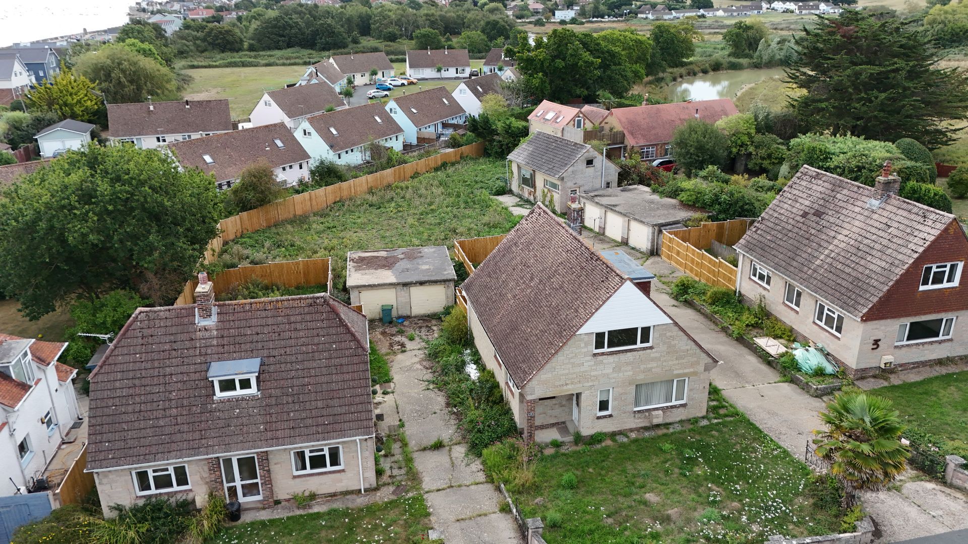 Aerial view of houses with brown roofs, green yards, and overgrown vegetation in a residential area.
