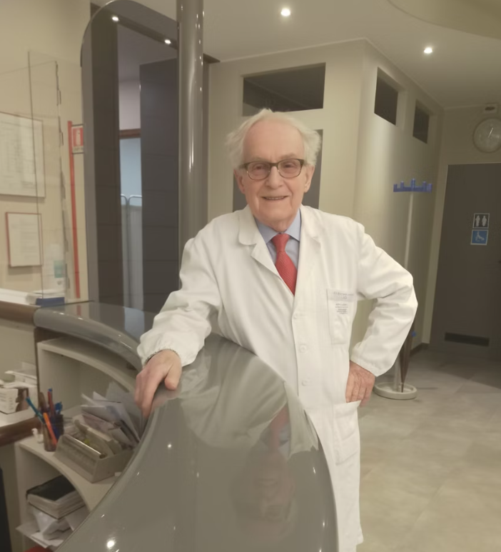 Un medico in camice bianco è in piedi davanti a un bancone curvo della reception. Ambiente da ufficio.