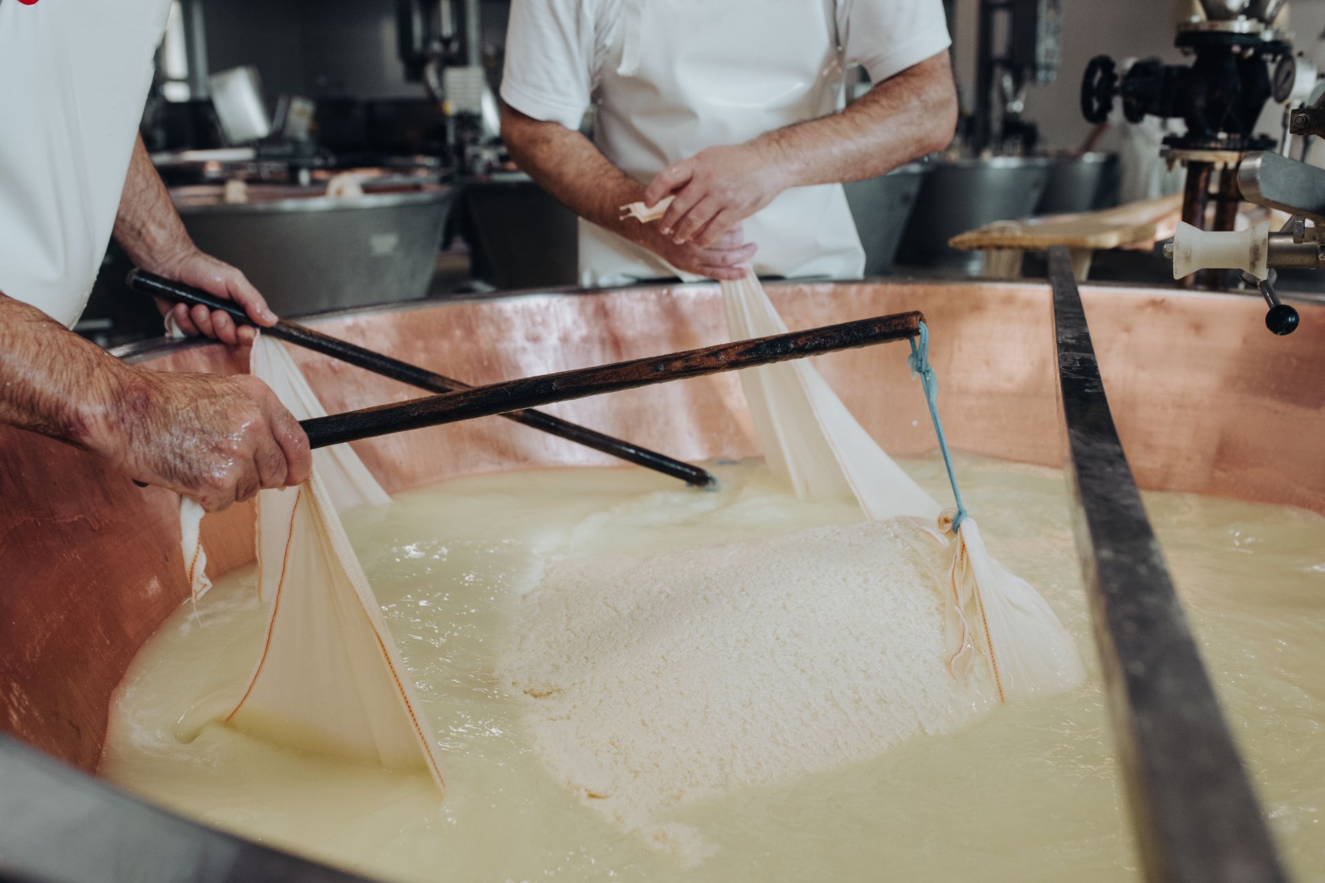 Due persone mescolano la cagliata di formaggio in una grande vasca di rame dotata di reti.