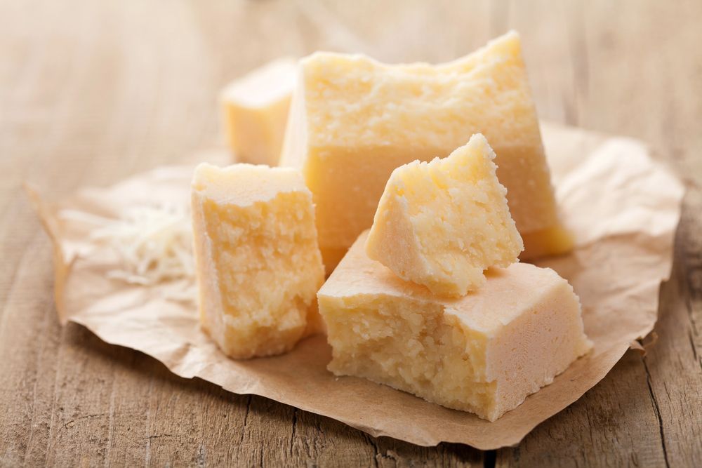 Pezzi di parmigiano su carta marrone, tavolo di legno.