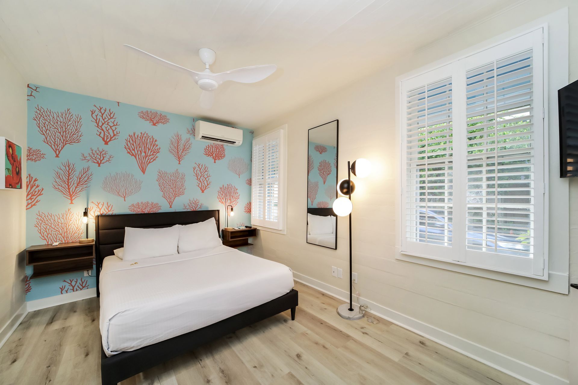 Bedroom with a blue coral-patterned accent wall, a bed, a window with shutters, and a standing lamp.