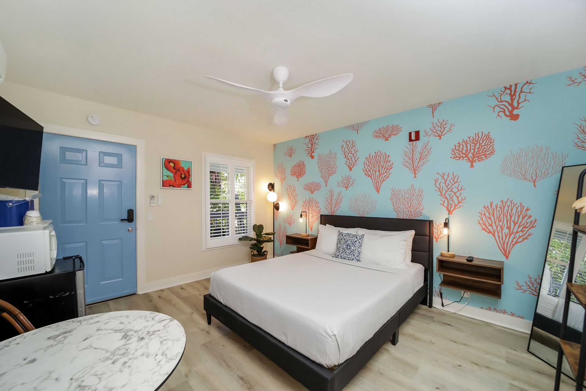 Bedroom with a bed, coral-patterned accent wall, blue door, and small round table.