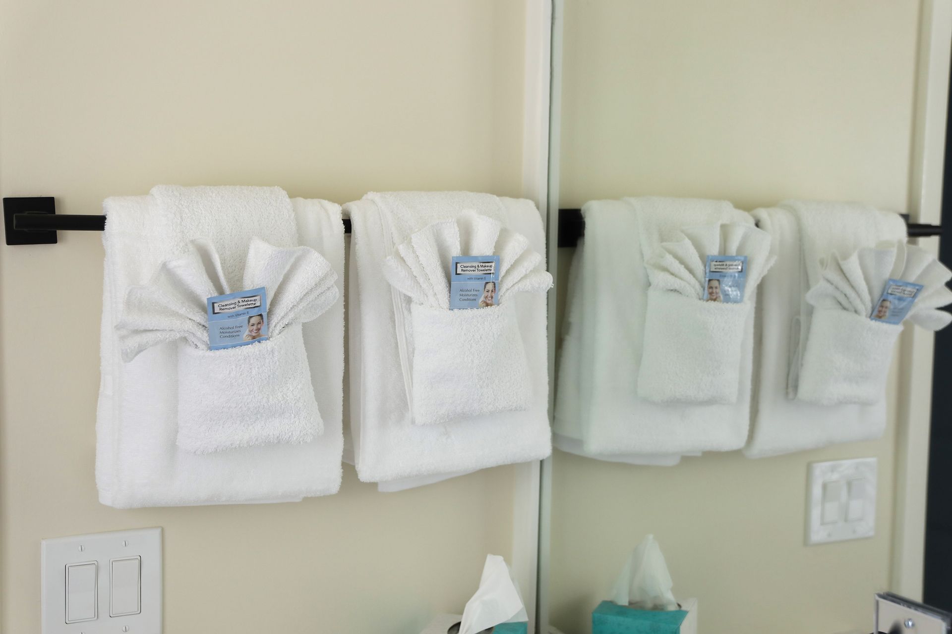 White towels folded on a black bar above a mirror, with small packets in the folds.