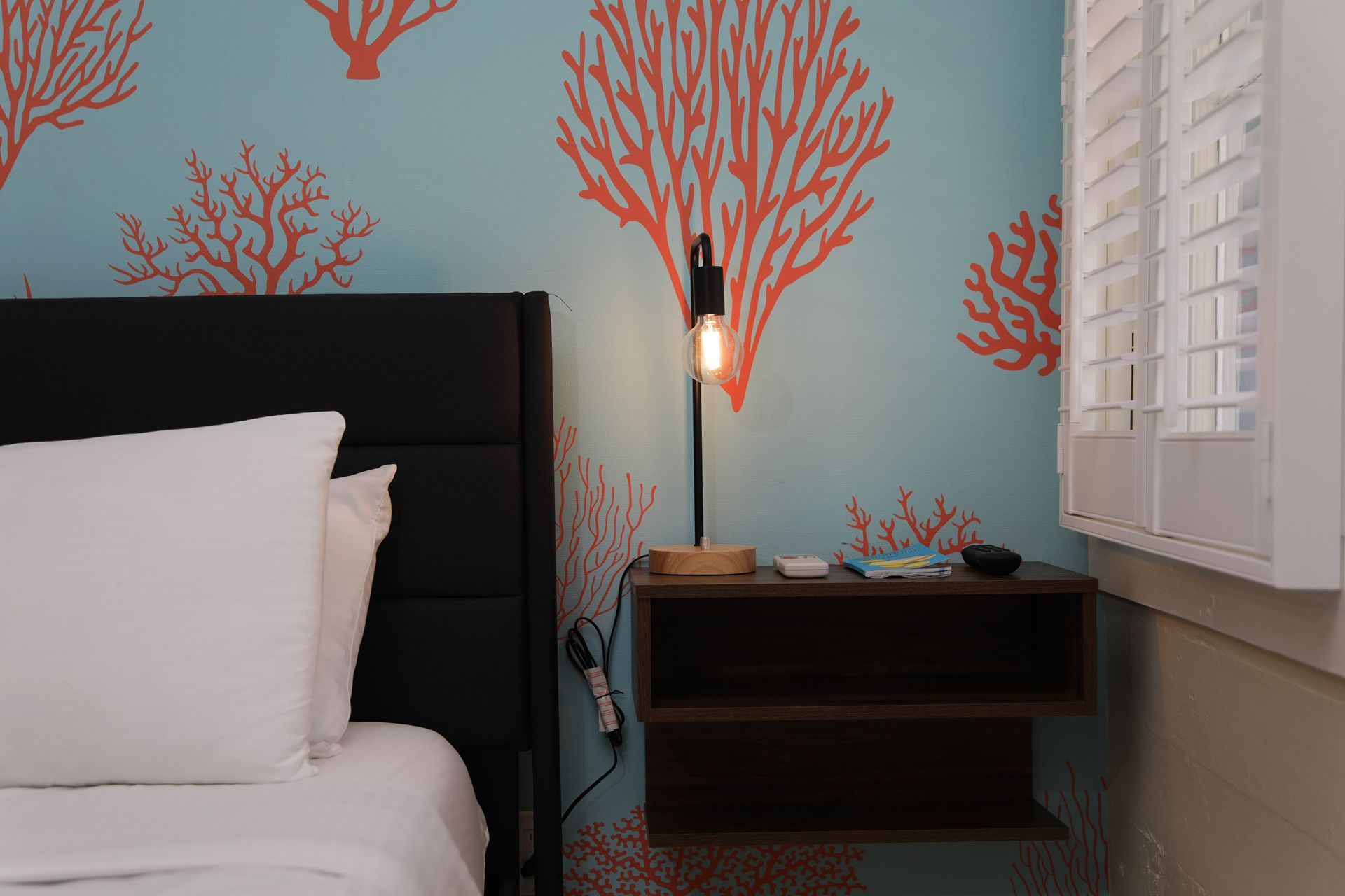 Bed with black headboard, nightstand with lamp, and coral-patterned blue wall.