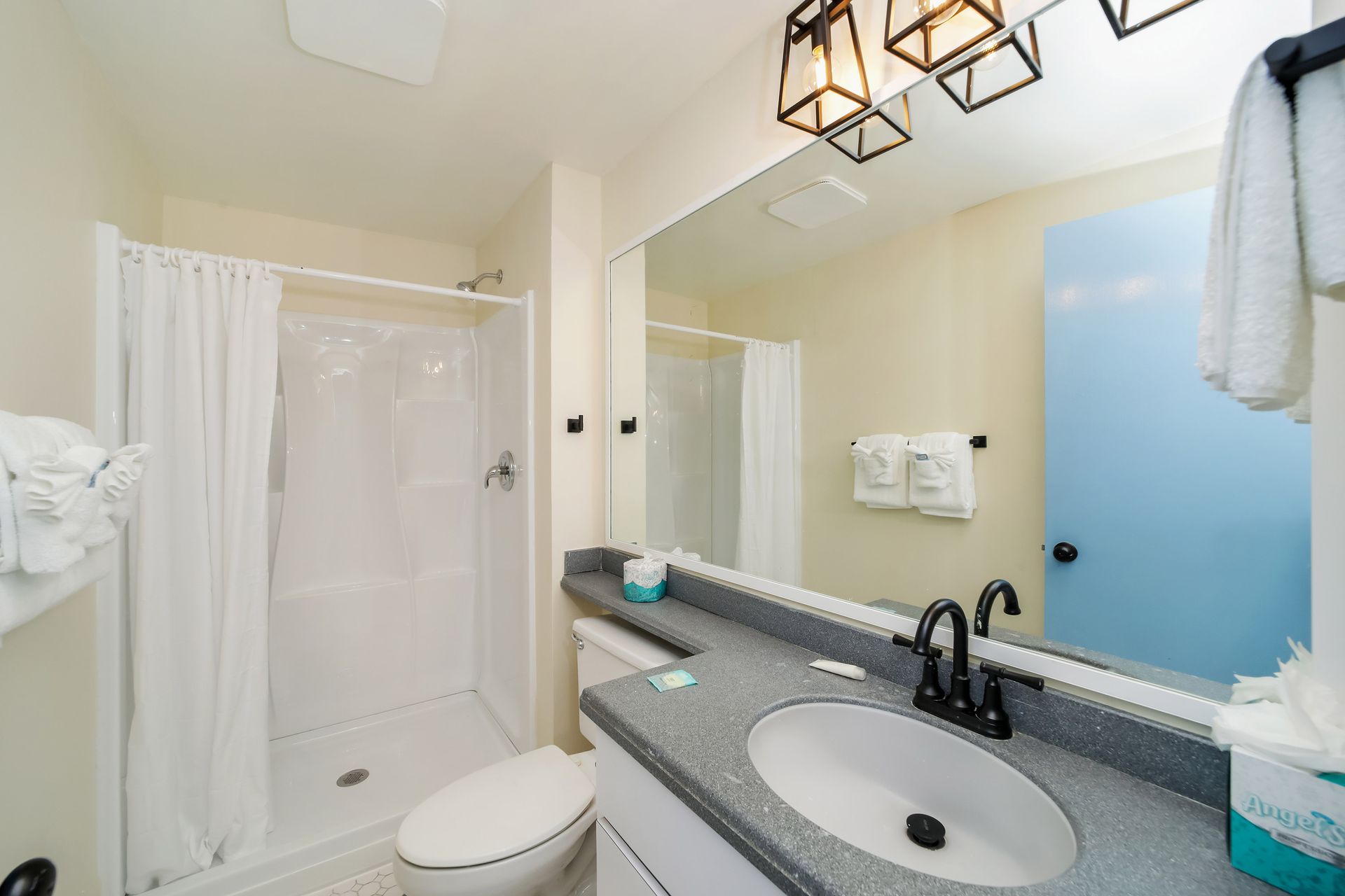 Bathroom with a shower, toilet, sink, mirror, and towels. Light blue door and neutral walls.