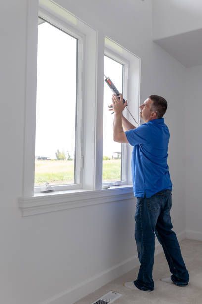 Men seals energy-efficient window with caulk during professional window replacement services.