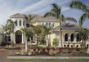 Large yellow house with palm trees, a circular driveway, and a flowerbed.