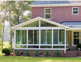 A brick house with a sunroom addition with glass windows, sitting on a green lawn.