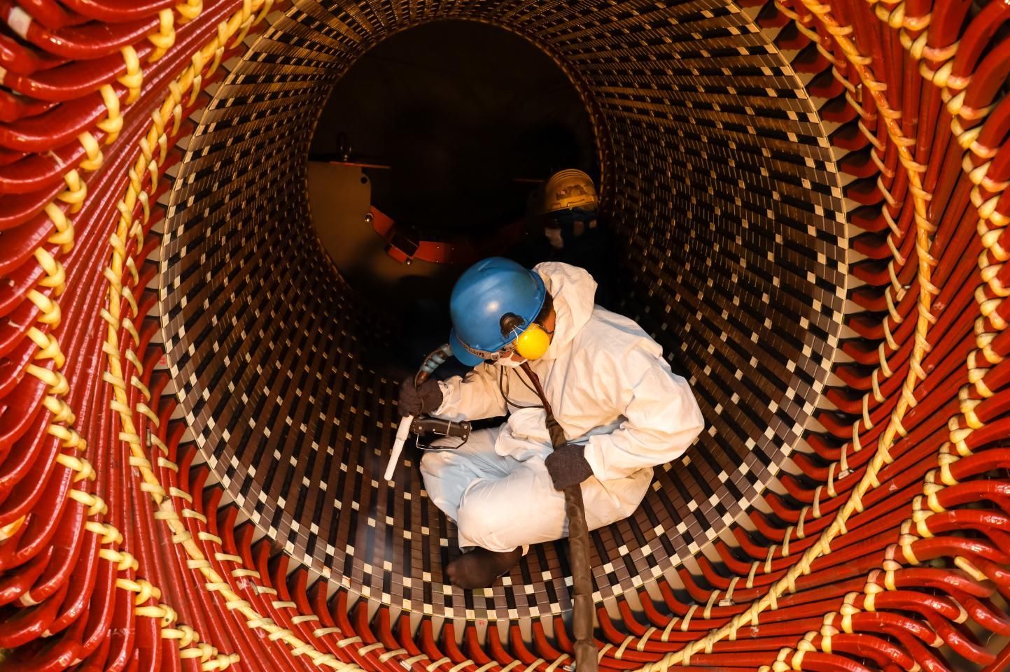 Worker inside a large electric motor stator, wearing protective gear, inspecting the wiring.