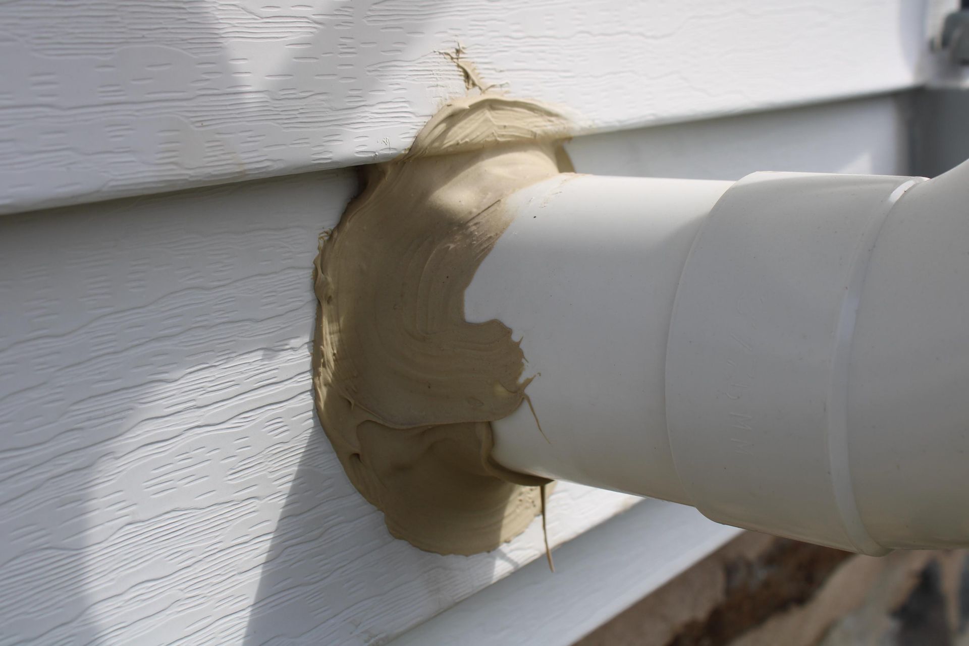 White PVC pipe extending from a siding wall, sealed with beige caulk.