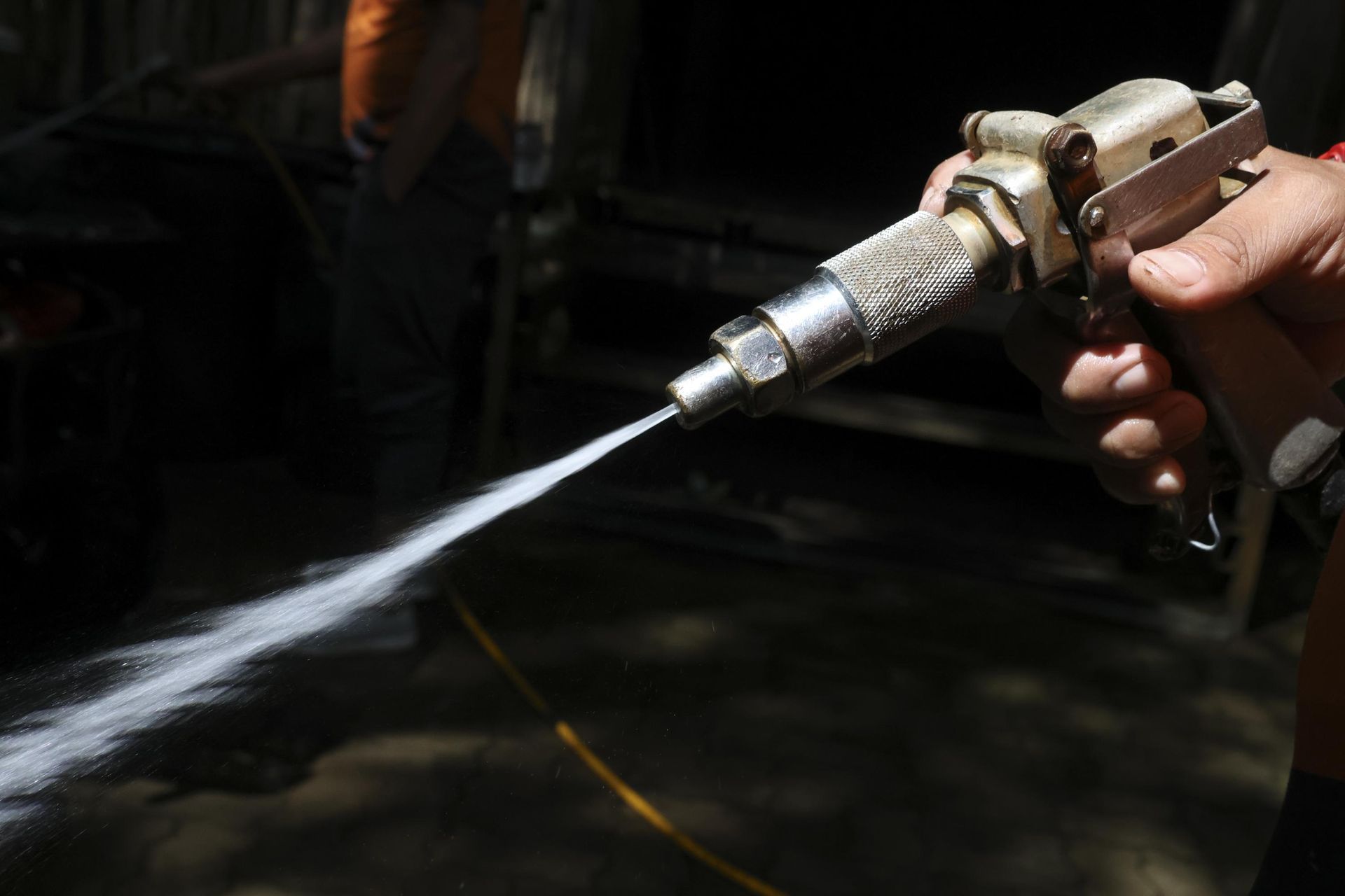 Hand holding a spray gun, emitting a stream of white substance.