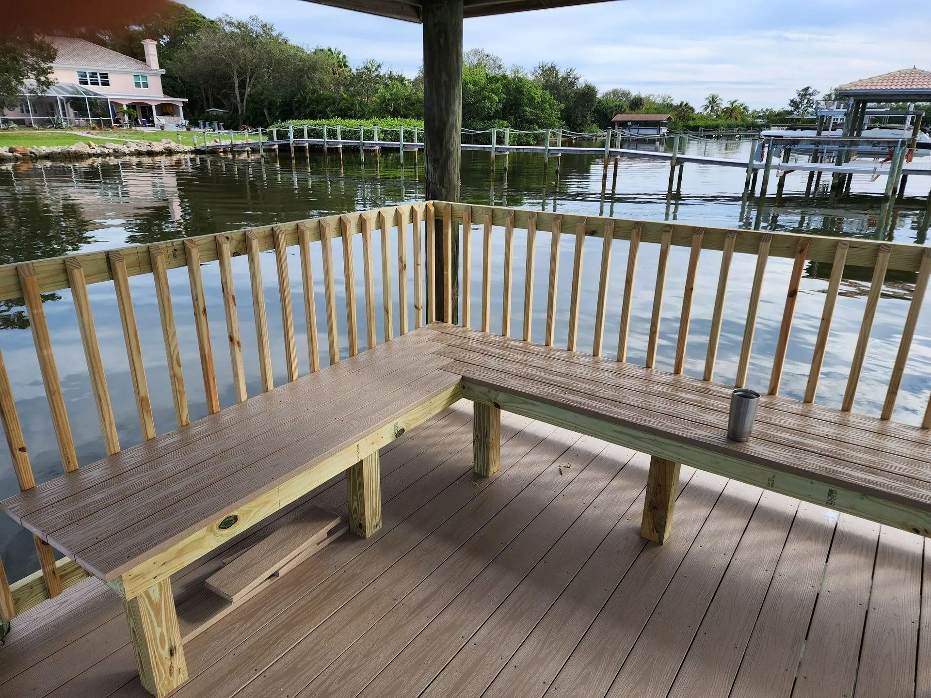 A wooden dock with an L-shaped bench overlooking a waterway. The scene is bathed in natural light.