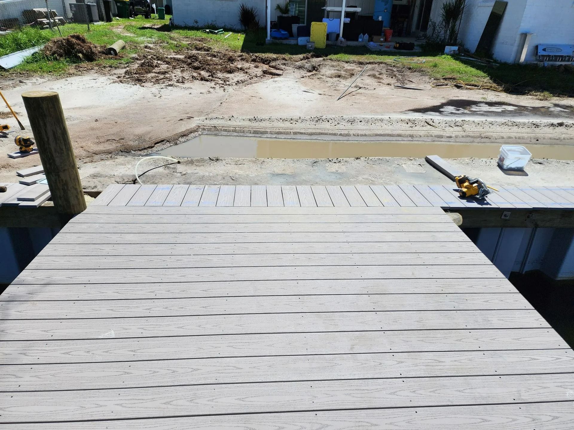 Wooden dock extending over a muddy area, with a house in the background.