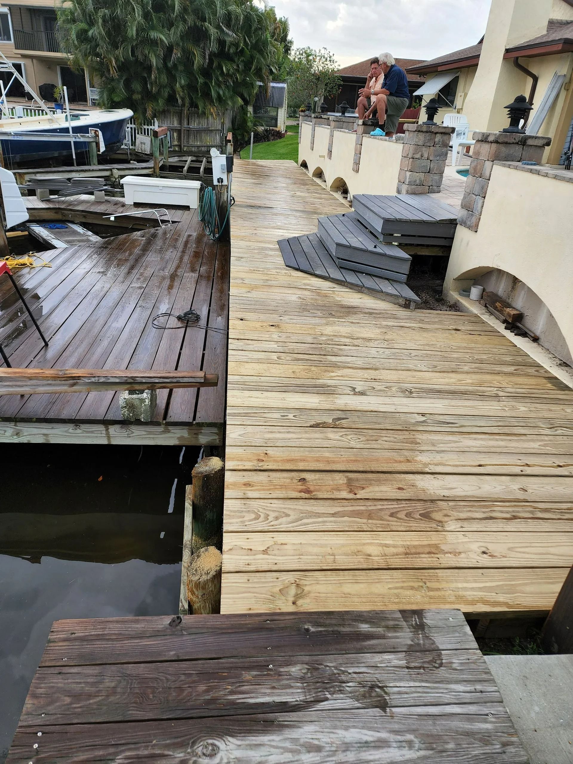 Wooden dock with a weathered appearance next to a water channel and a partially visible building with stone accents.